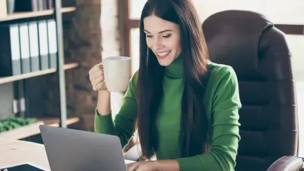 A woman in a green shirt sits at a laptop in front of a bookshelf